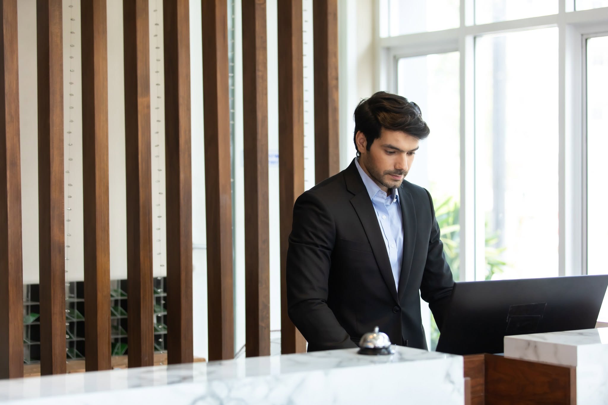 Friendly handsome man hotel receptionist in a stylish luxury hotel welcome and helping a female client at the front desk